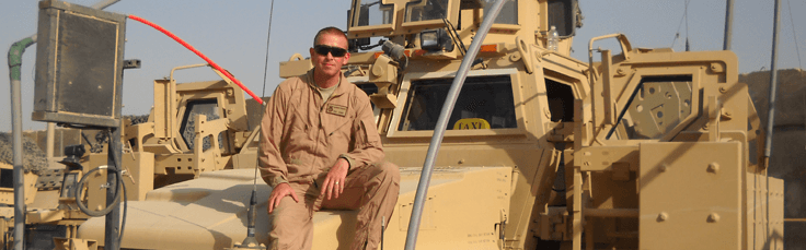 Damien Foord in uniform, sitting on an armored vehicle in Iraq.
